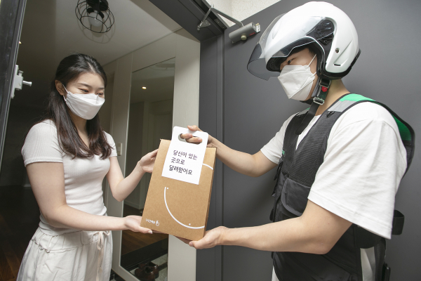 KT 고객이 자택에서 ‘1분주문 & 1시간배송’ 서비스를 이용해 주문한 핸드폰을 부릉 라이더로부터 배송 받고 있다. / 사진 = KT 제공