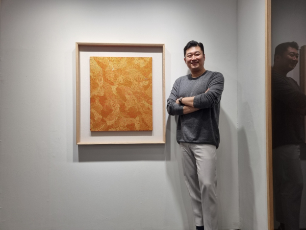 김재욱 열매컴퍼니 대표가 '야요이 쿠사마, Nets, 1999, Acrylic on canvas, 73x61cm' 옆에서 포즈를 취하고 있다./ 사진=최다은 기자