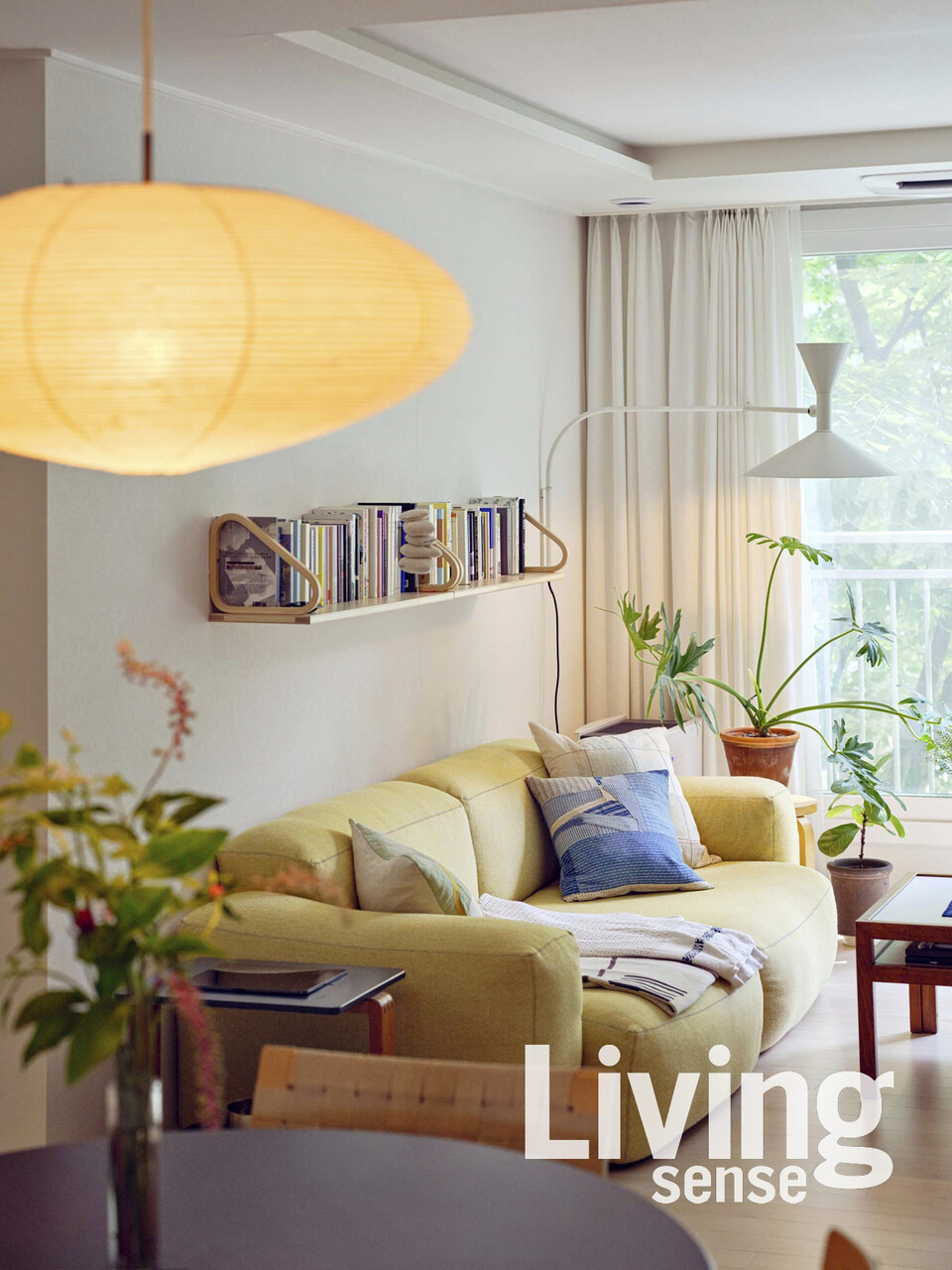 책을 정갈하게 꽂아 넣은 아르텍 벽선반이 흰 벽의 포인트가 되어주는 거실. 텍스타일 아티스트 사라 에스푀트Sarah Espeute 의 자수 쿠션, 교토 편집숍 브라운교토Brownkyoto에서 구매한 빈티지 데님 쿠션에서 부부의 취향을 엿볼 수 있다. 