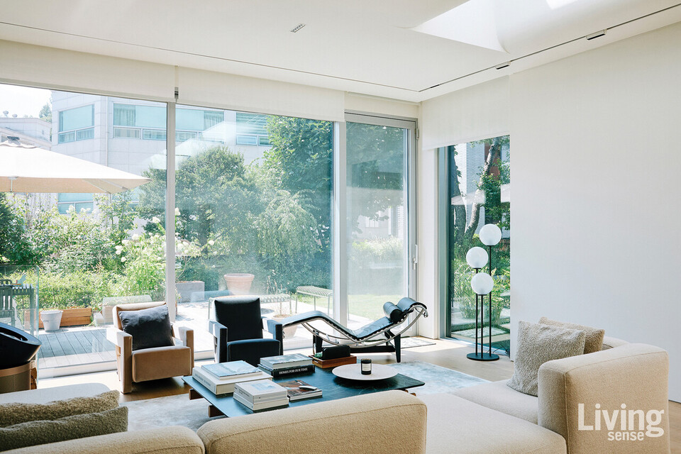 큰 창을 통해 정원의 초록과 빛이 스며드는 거실. 르 코르뷔지에의 데이베드와 미니멀한 가구들이 놓인 공간은 휴식과 풍경을 함께 즐기는 장면을 완성한다.