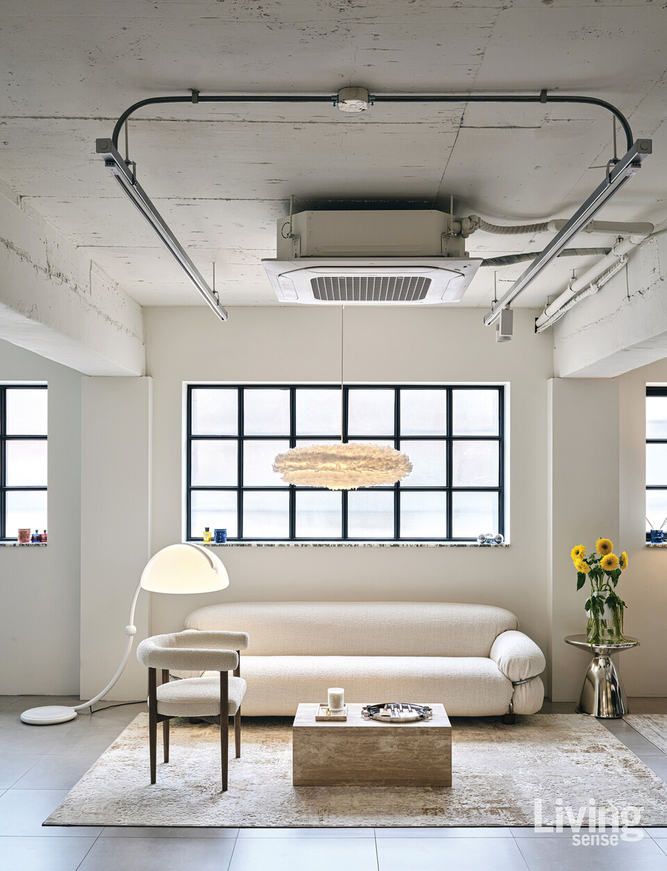 거실에는 포근한 느낌의 소파와 낮게 떨어지는 조명, 블랙 프레임의 창문, 천장의 자연스러운 노출이 조화롭게 어울린다.