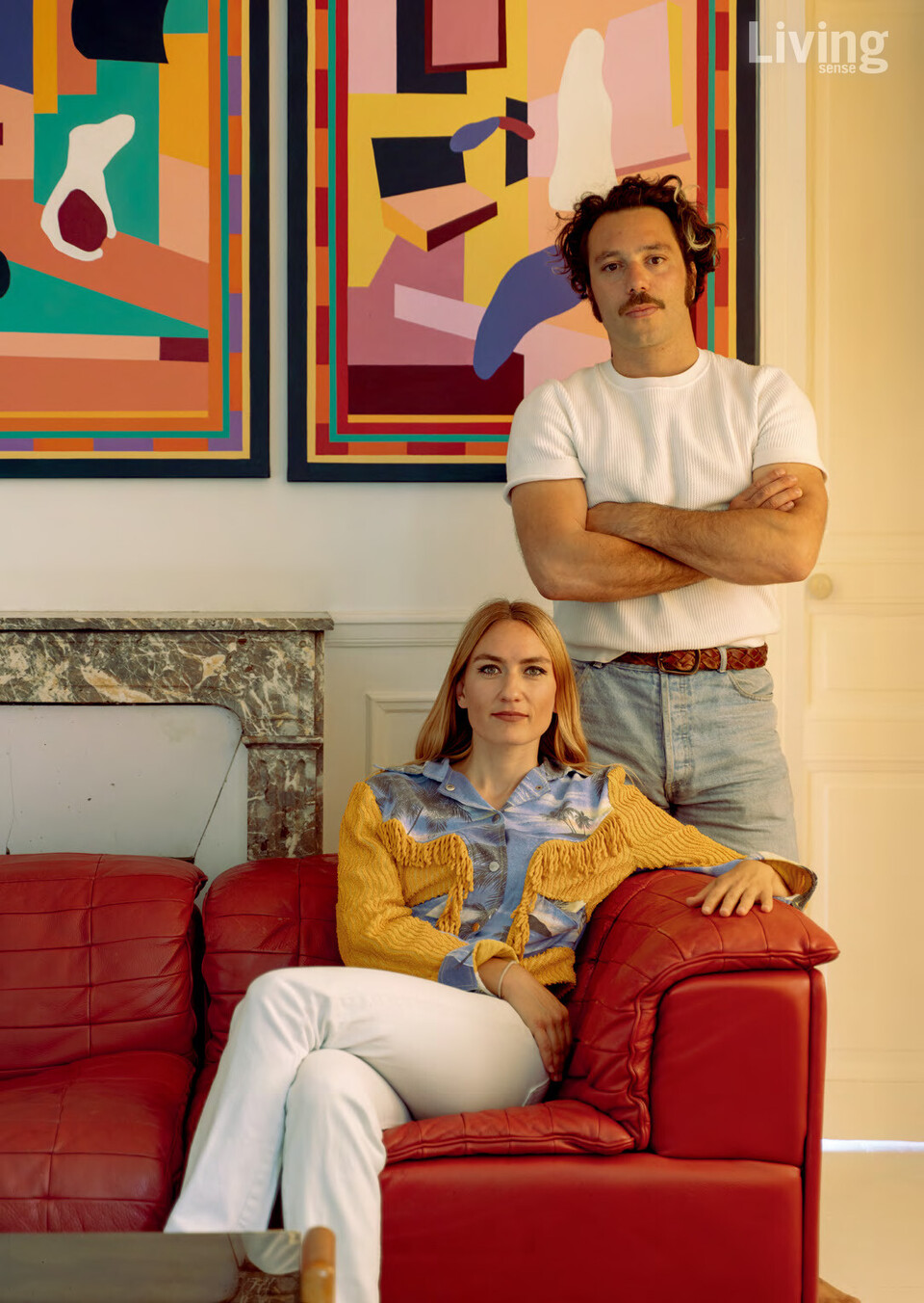 드 세데의 새빨간 소파에 앉은 화가 캐롤라인 데르보와 그 뒤에 서 있는 건축가 위고 뱅스.